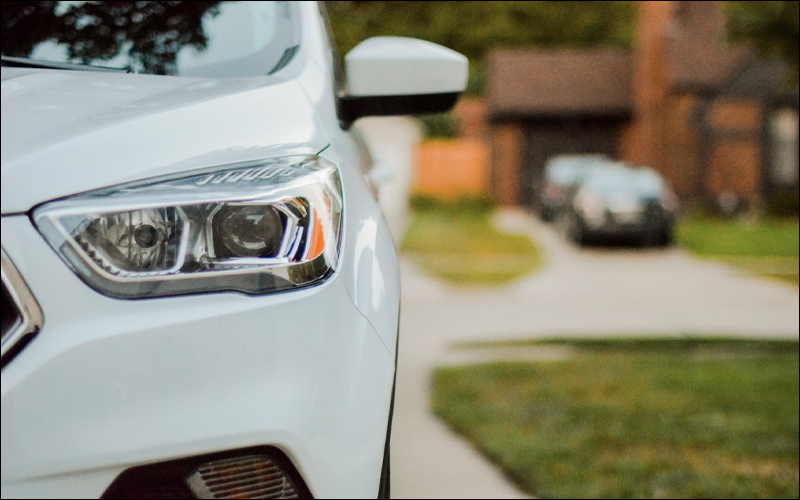 White car parked in driveway with another house in view behind it.