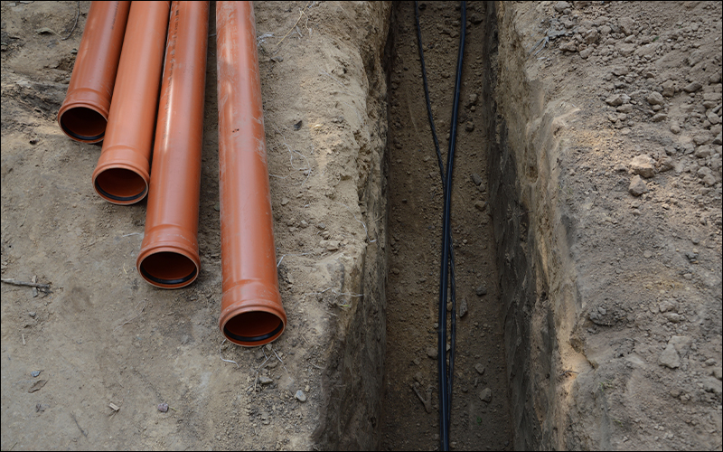 Plastic pipes laying on dirt and internet wires inside trench.