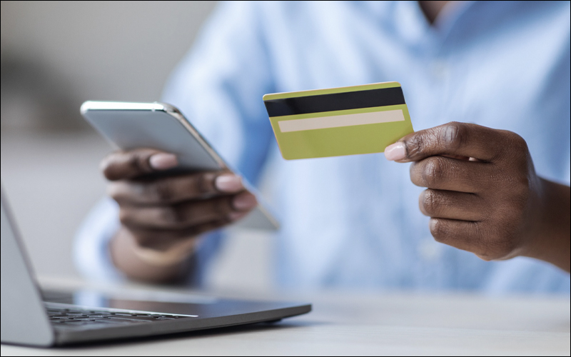 Person holding credit card and phone, sitting in front of laptop.