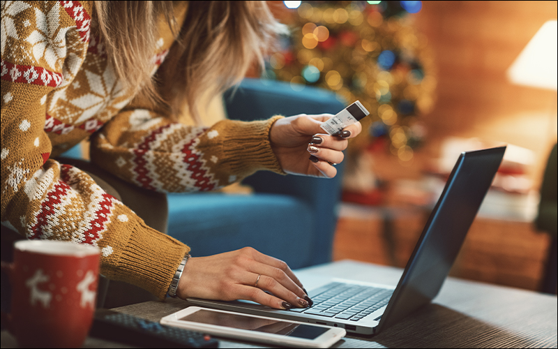 Person with holiday sweater on using credit card to order online.