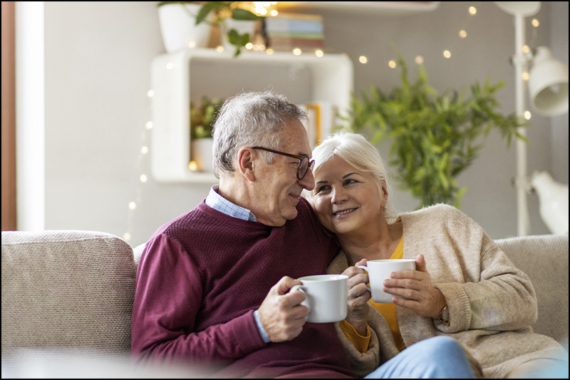 Retired couple sitting on couch holding mugs.