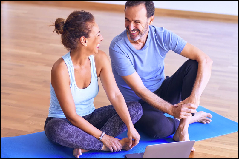 Couple sitting on yoga mat with laptop in front of them.