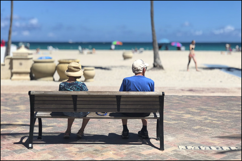 Two people sitting on a bench at a beach with their backs to the camera.