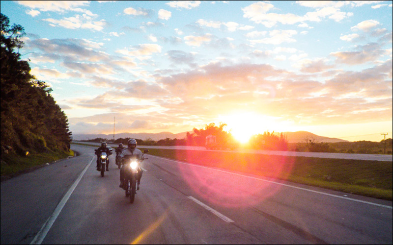 Motorcyclists on road with sunset behind them.