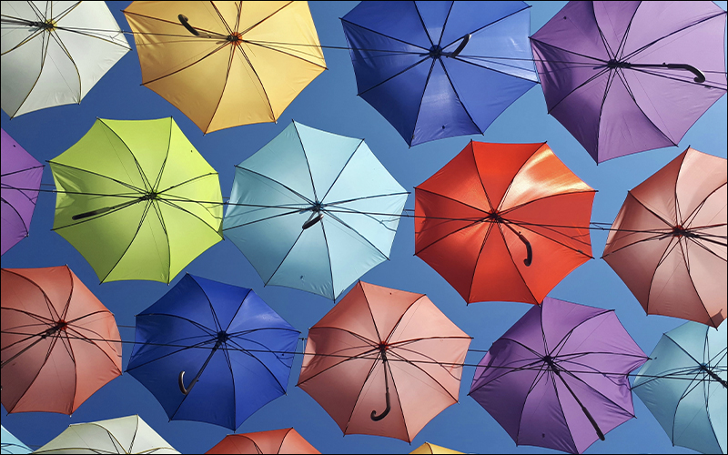 Looking up at a bunch of umbrellas with blue sky behind them.