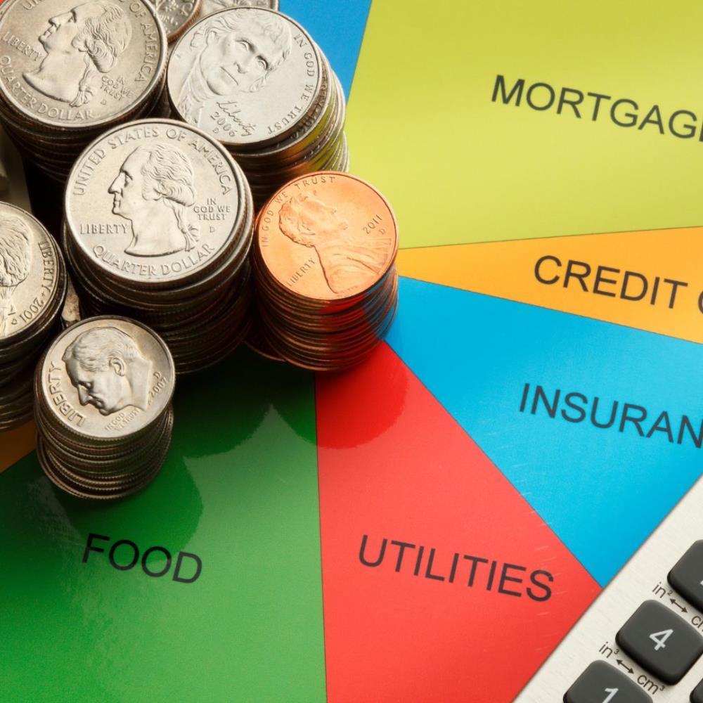 A stack of coins and a calculator on a pie chart depicting the make up of typical household expenses