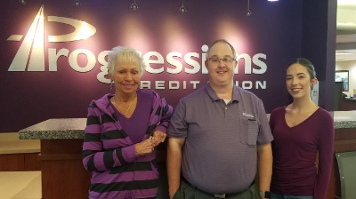 2 women and 1 man in front of progressions credit union sign