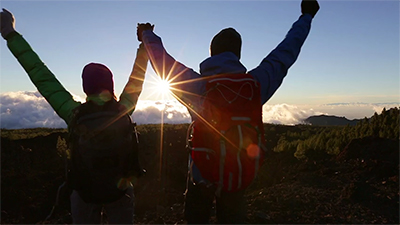 couple holding arms up while viewing a sunset from a mountain top